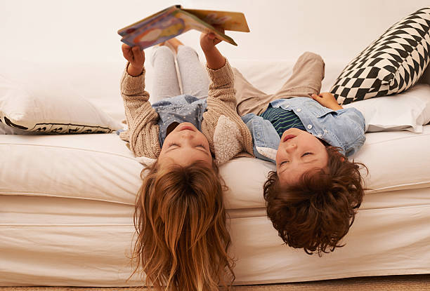shot of two young children lying on their backs and reading a book together